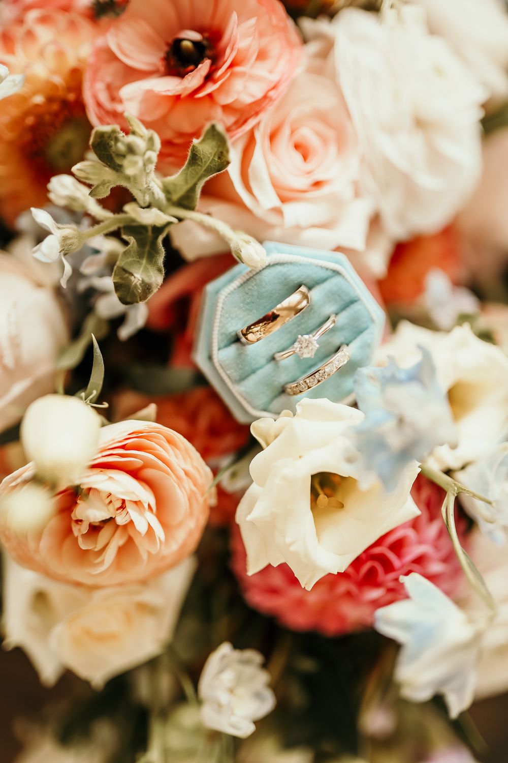 Wedding rings displayed on a blue velvet cushion among coral and white flowers.