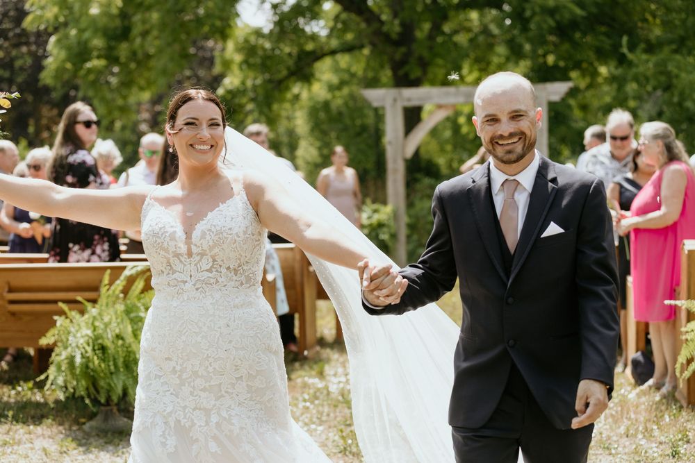 A wedding couple holding hands and walking through an outdoor garden setting while guests look on with joy.