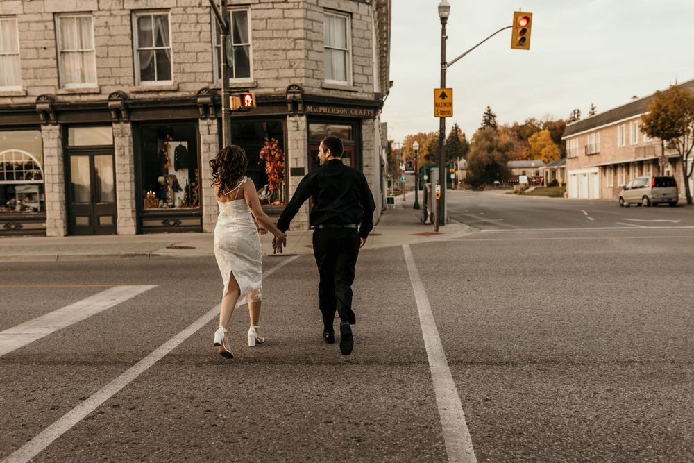 A couple running together on a city street with one wearing a flowing white dress.