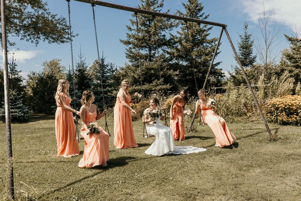 Wedding party having fun on playground swings with bride in white and bridesmaids in peach dresses.
