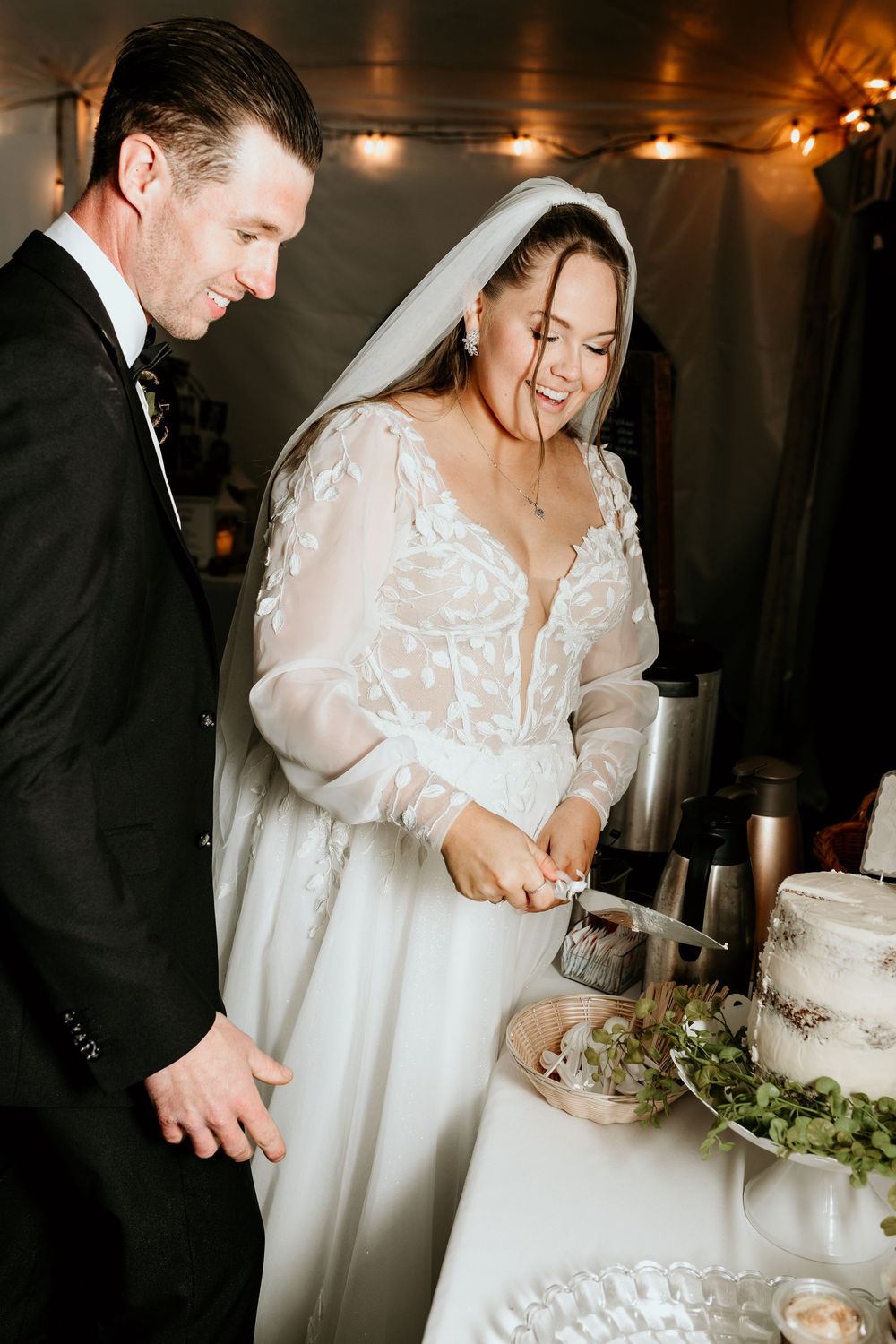 A couple in wedding attire cuts their wedding cake together during their reception celebration.