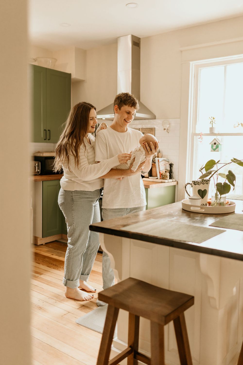 Couple enjoying morning coffee in modern kitchen with sage green cabinets and wooden flooring.