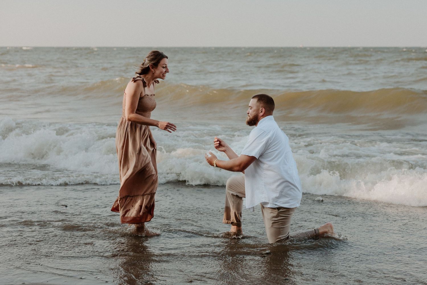 A romantic beach proposal scene with waves crashing in the background.