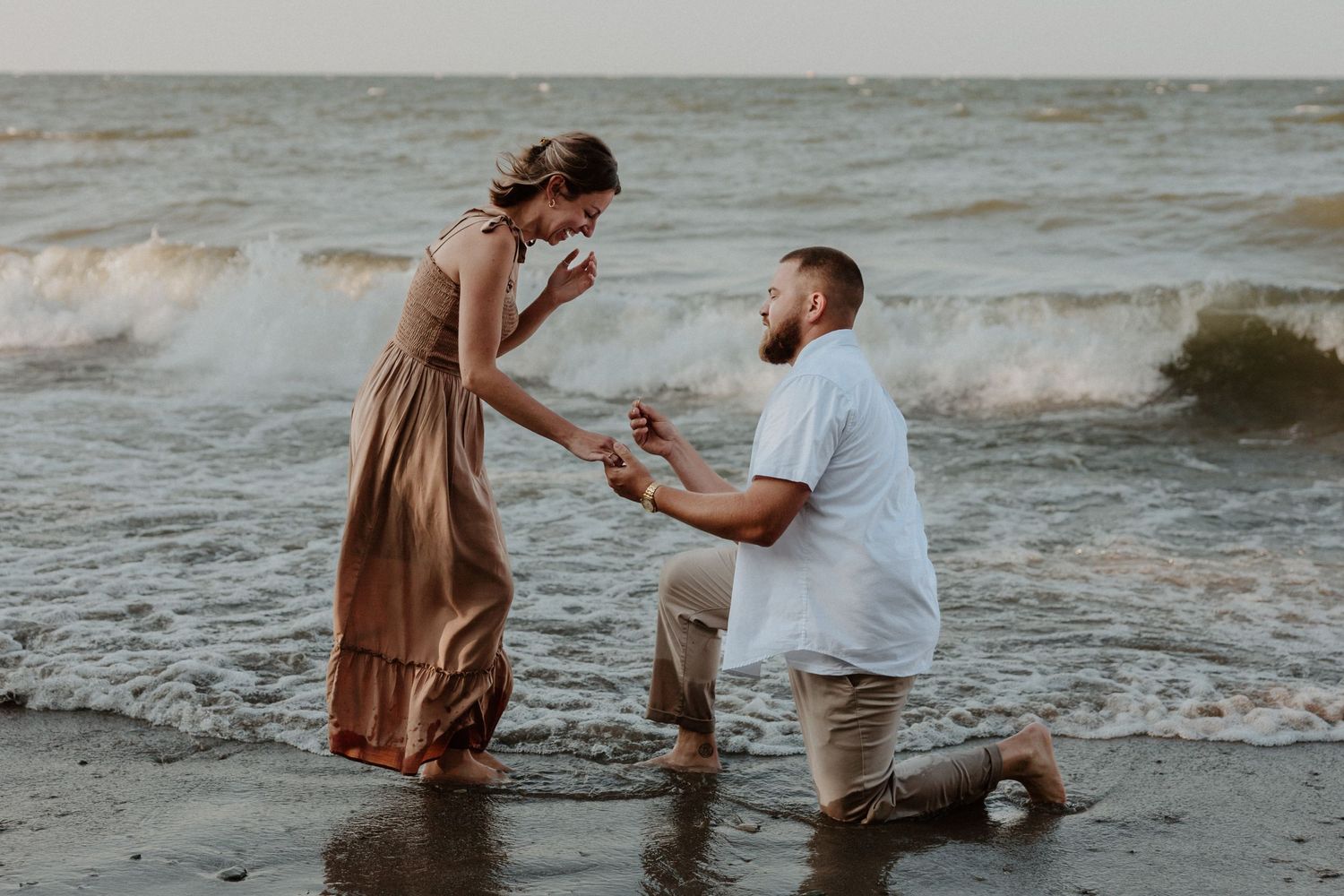 A couple shares a special moment during a beach proposal as waves crash behind them.