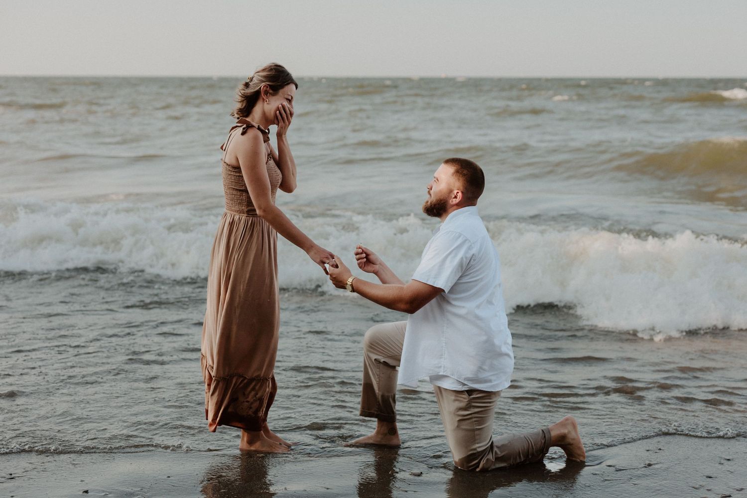 A romantic beach proposal scene with waves crashing in the background at sunset.