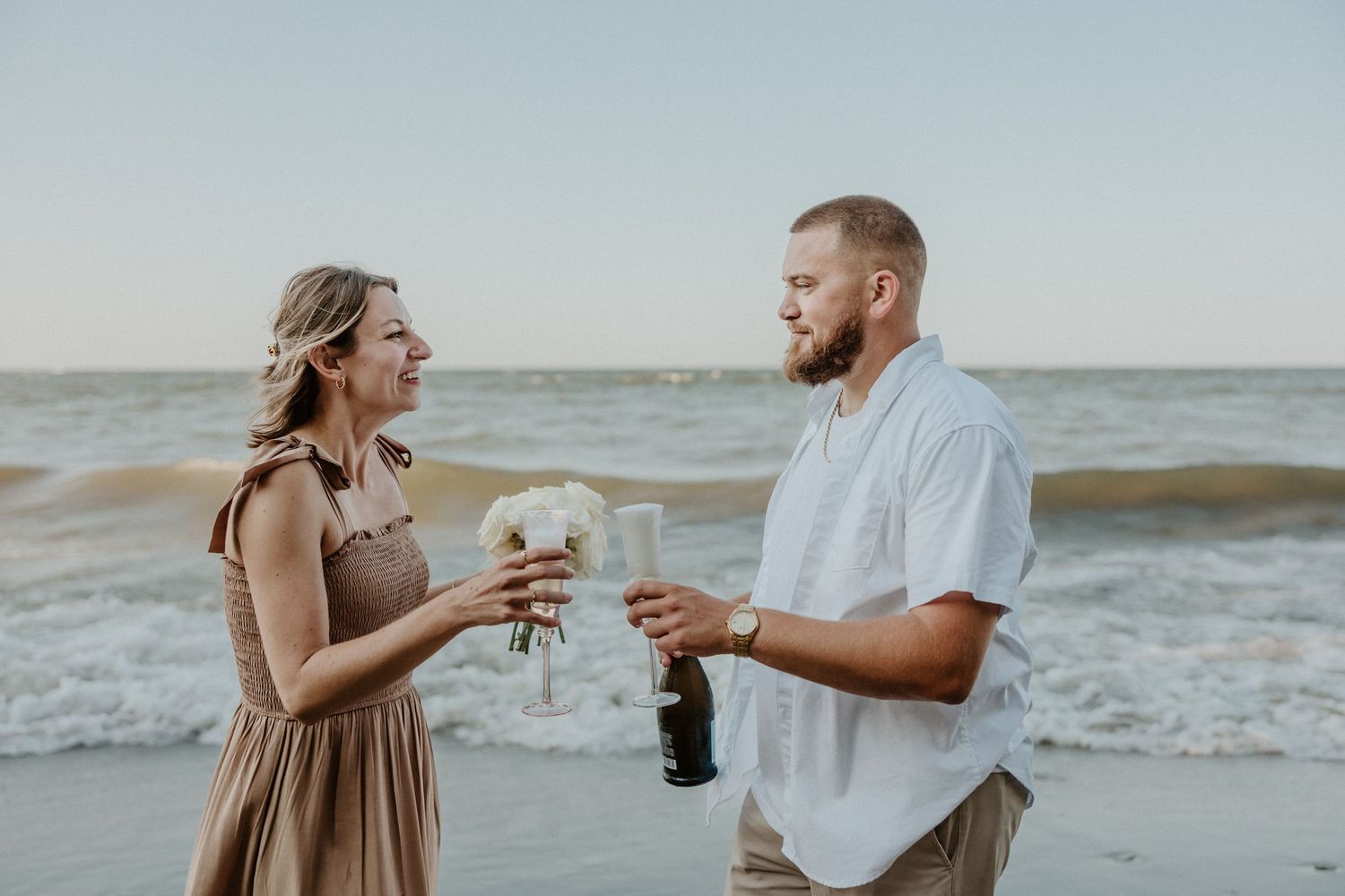 A couple celebrating with champagne on the beach after their engagement.