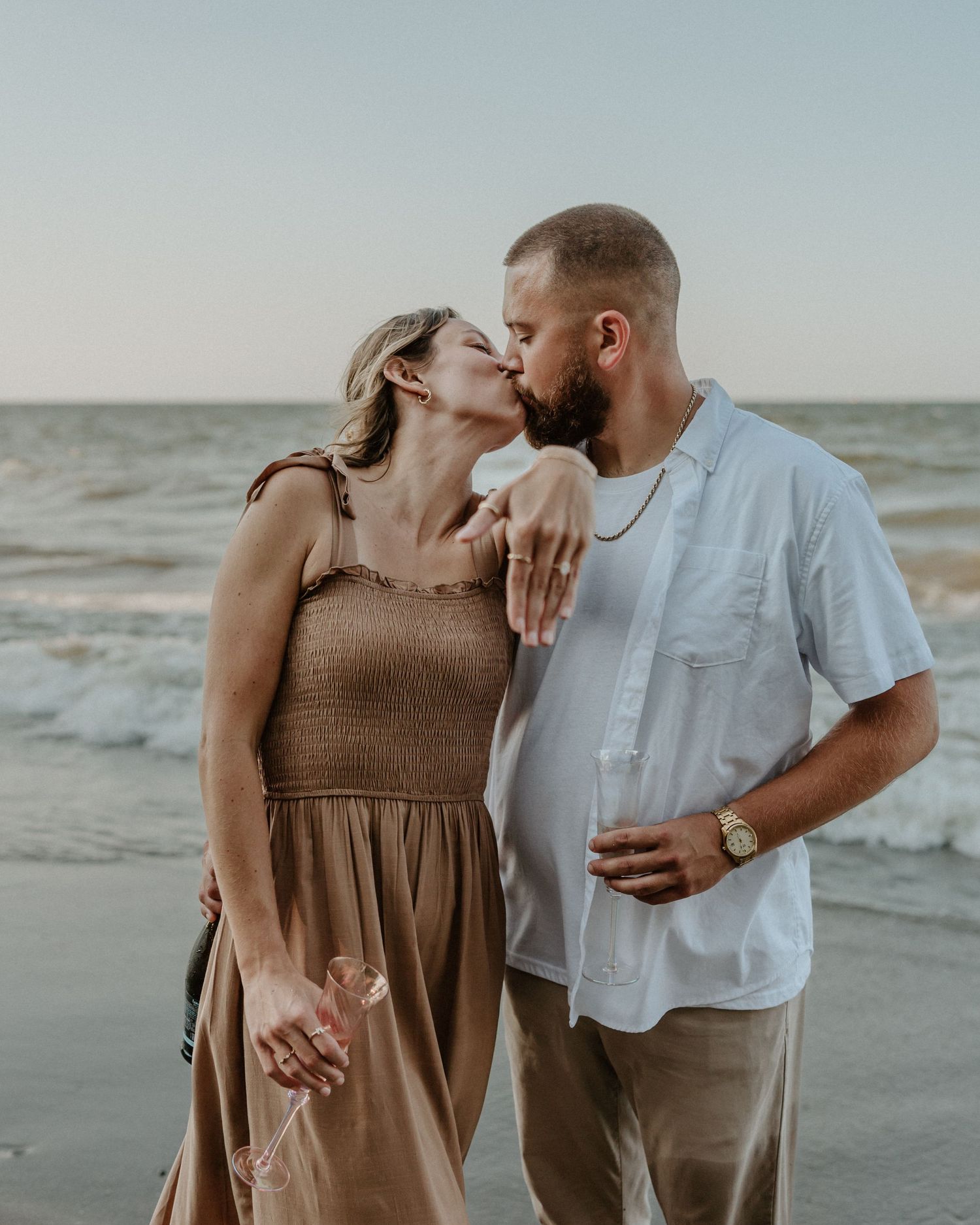 A romantic embrace shared between a couple on a sandy beach during golden hour.