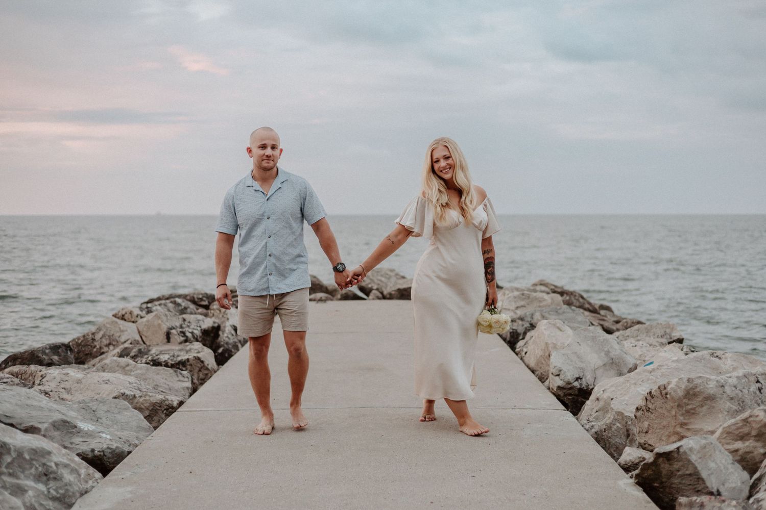 Couple walking hand in hand on concrete pier by the ocean.