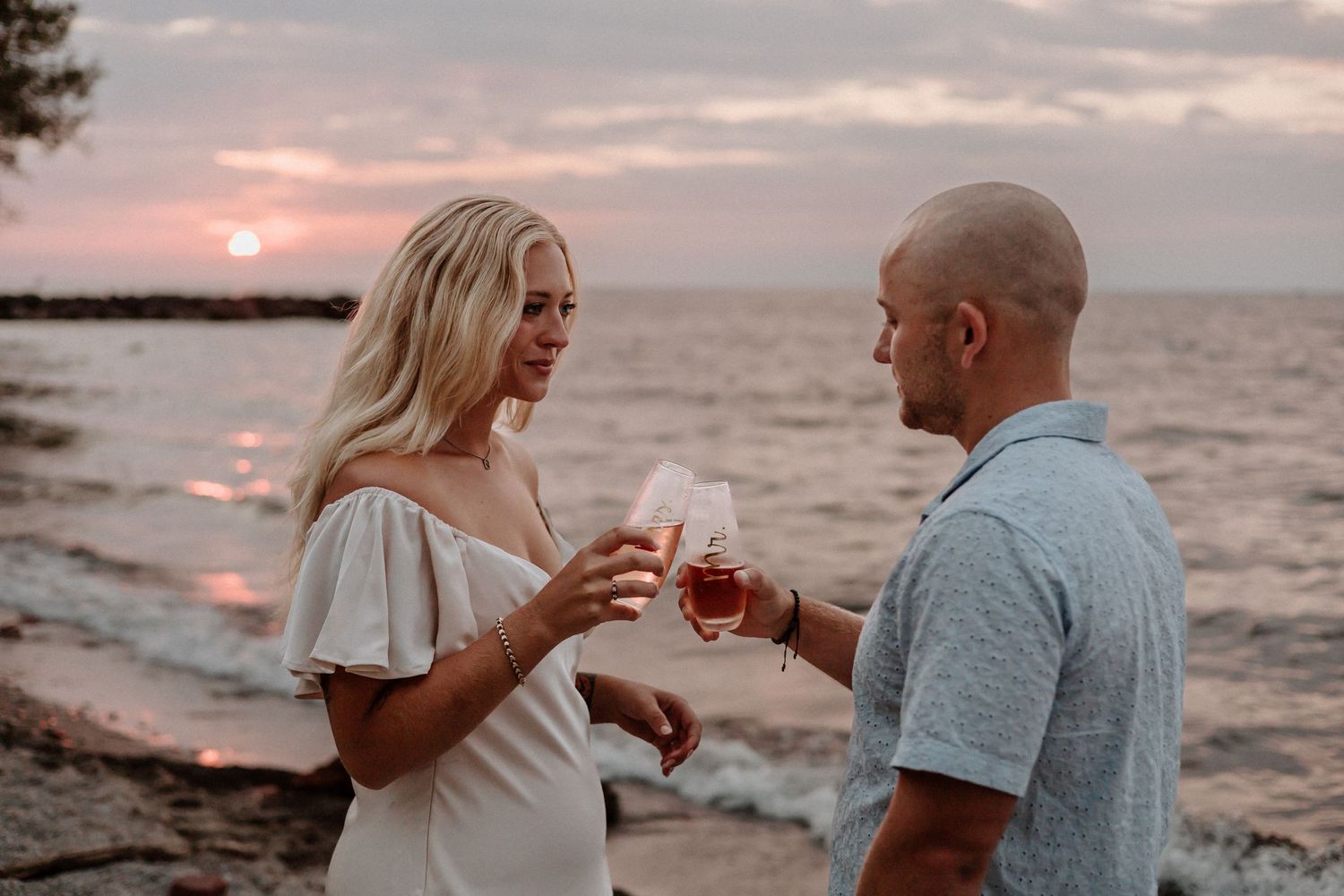 Couple sharing drinks together at sunset by the ocean.