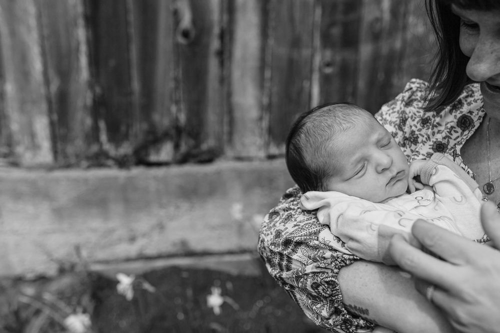 Black and white photo of a mother tenderly cradling her sleeping newborn baby close to her chest outdoors.