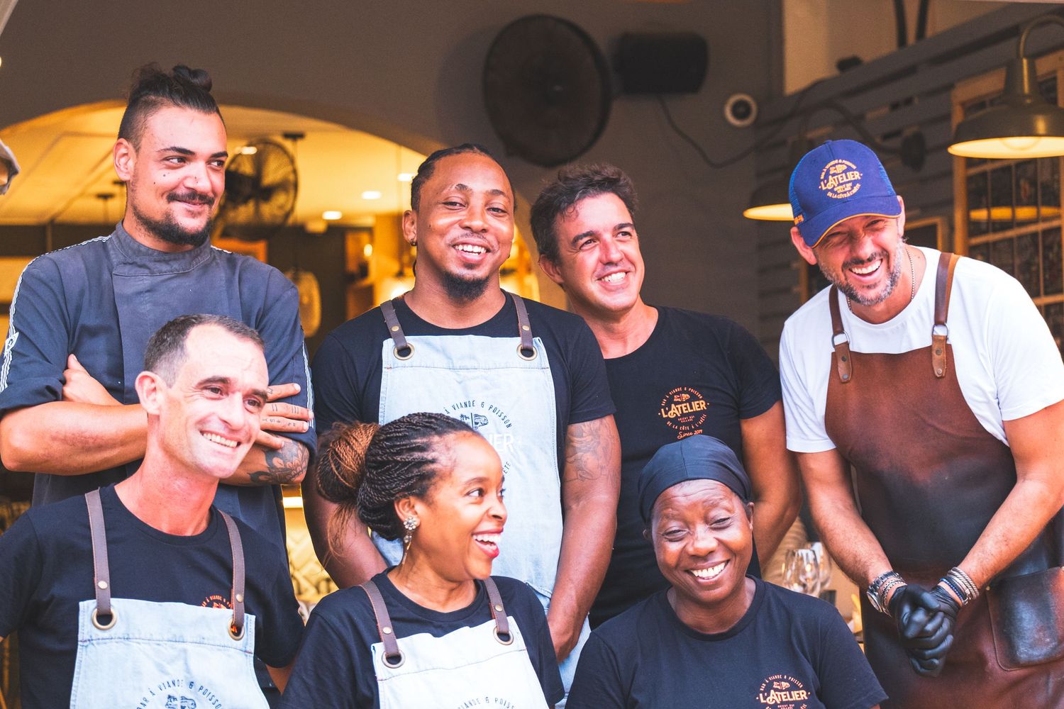 Smiling restaurant staff wearing aprons pose together in the kitchen for a group photo.