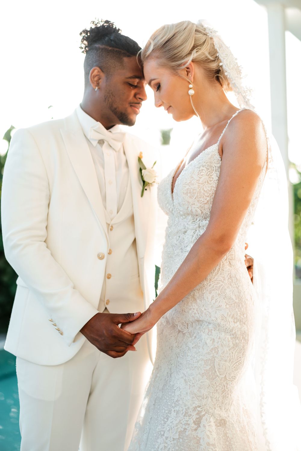 Intimate wedding couple portraits in white attire against bright backlit setting showing tender romantic moments.
