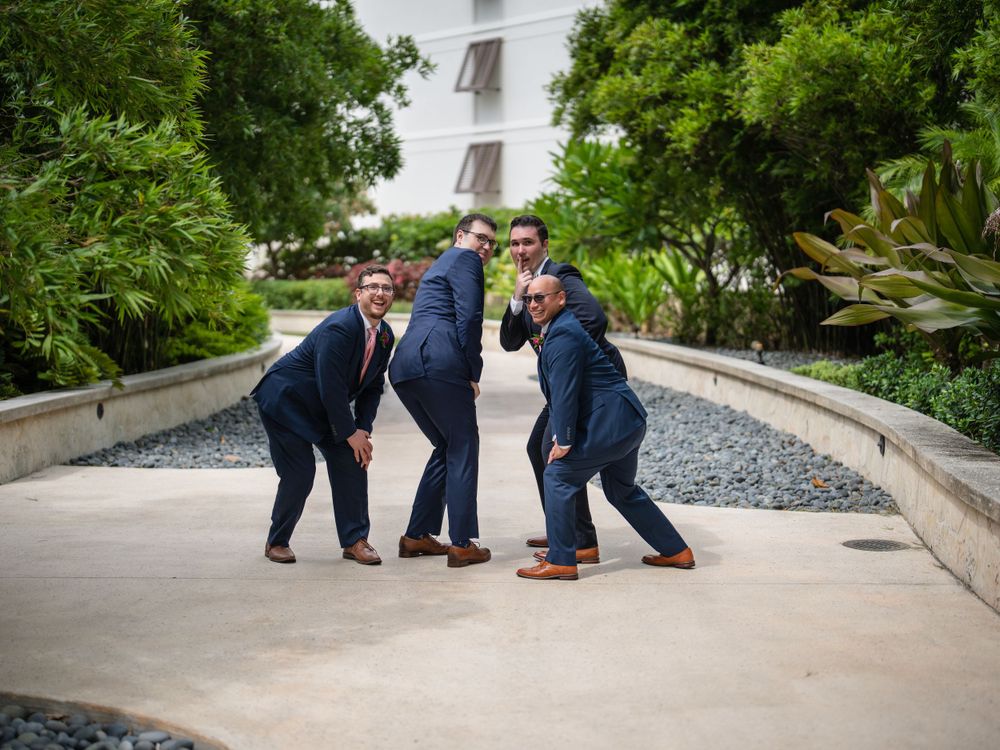 Groomsmen strike playful pose on pathway surrounded by greenery.