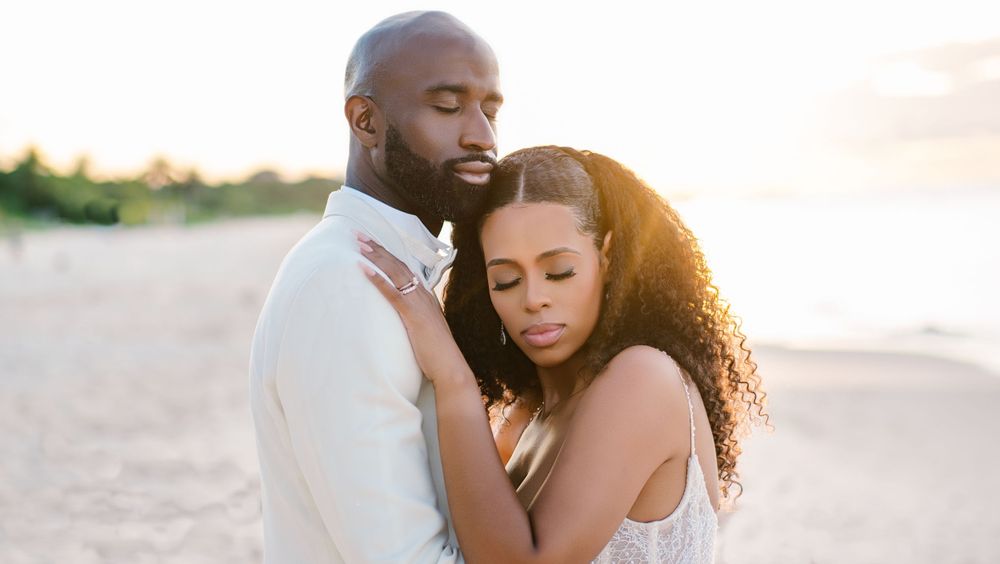 A romantic beach sunset portrait of a couple in white embracing on the sand.