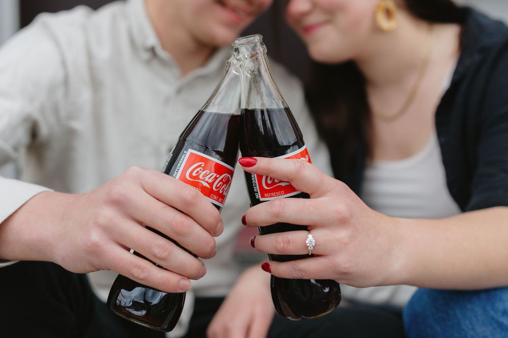 Two glass Coca-Cola bottles clinking together in a celebratory toast between two people.
