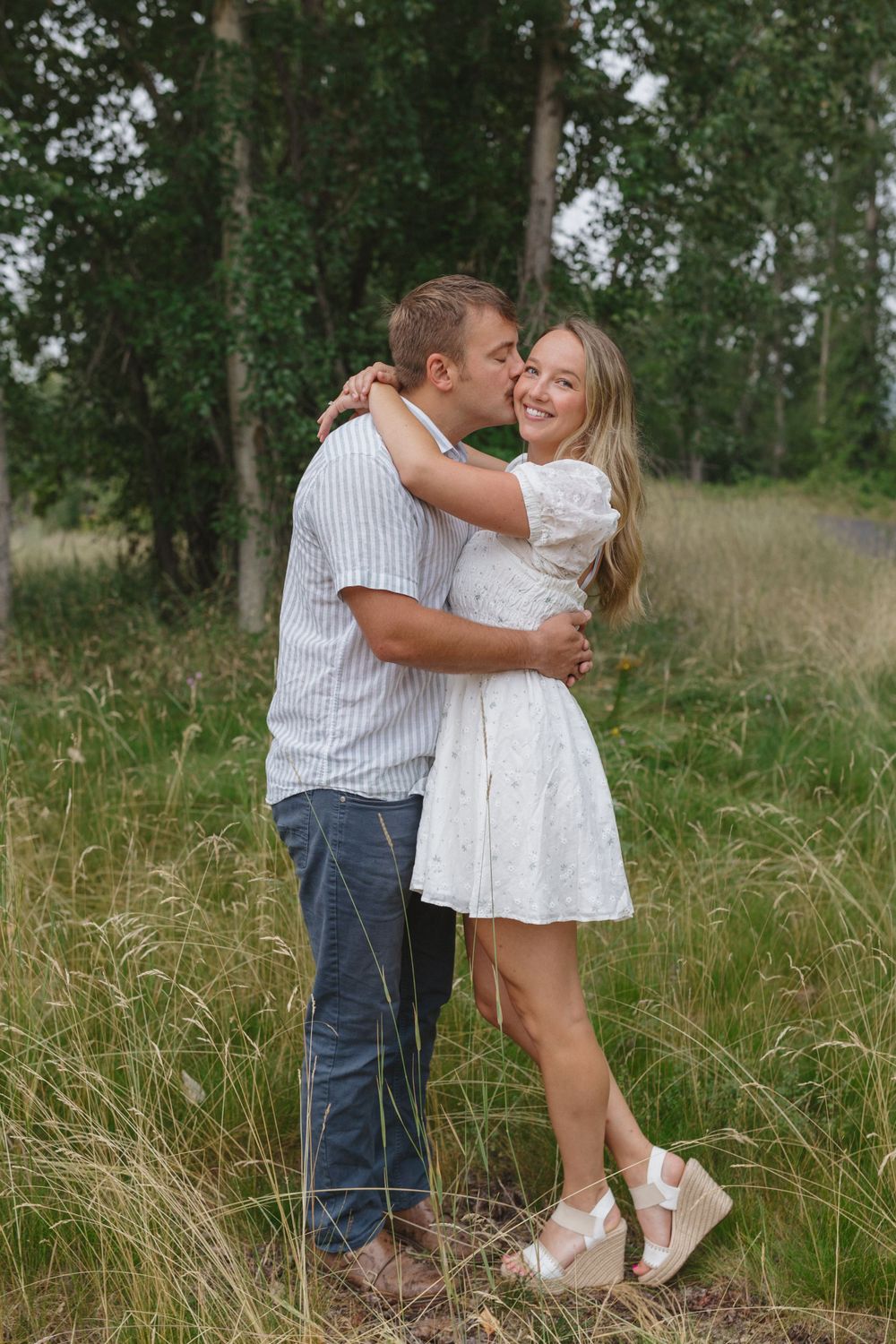 A romantic embrace between a couple standing in tall grass with aspen trees in the background.