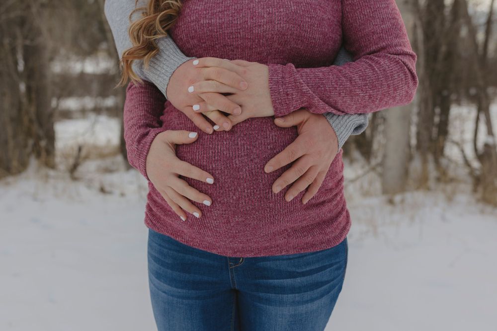 Close up view of someone wearing a burgundy sweater and jeans standing in snowy winter landscape.