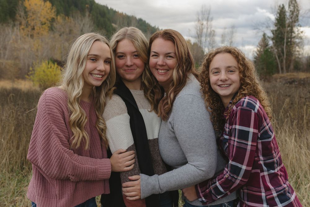A group of four people pose together outdoors on an autumn day with fall foliage and cloudy skies in the background.