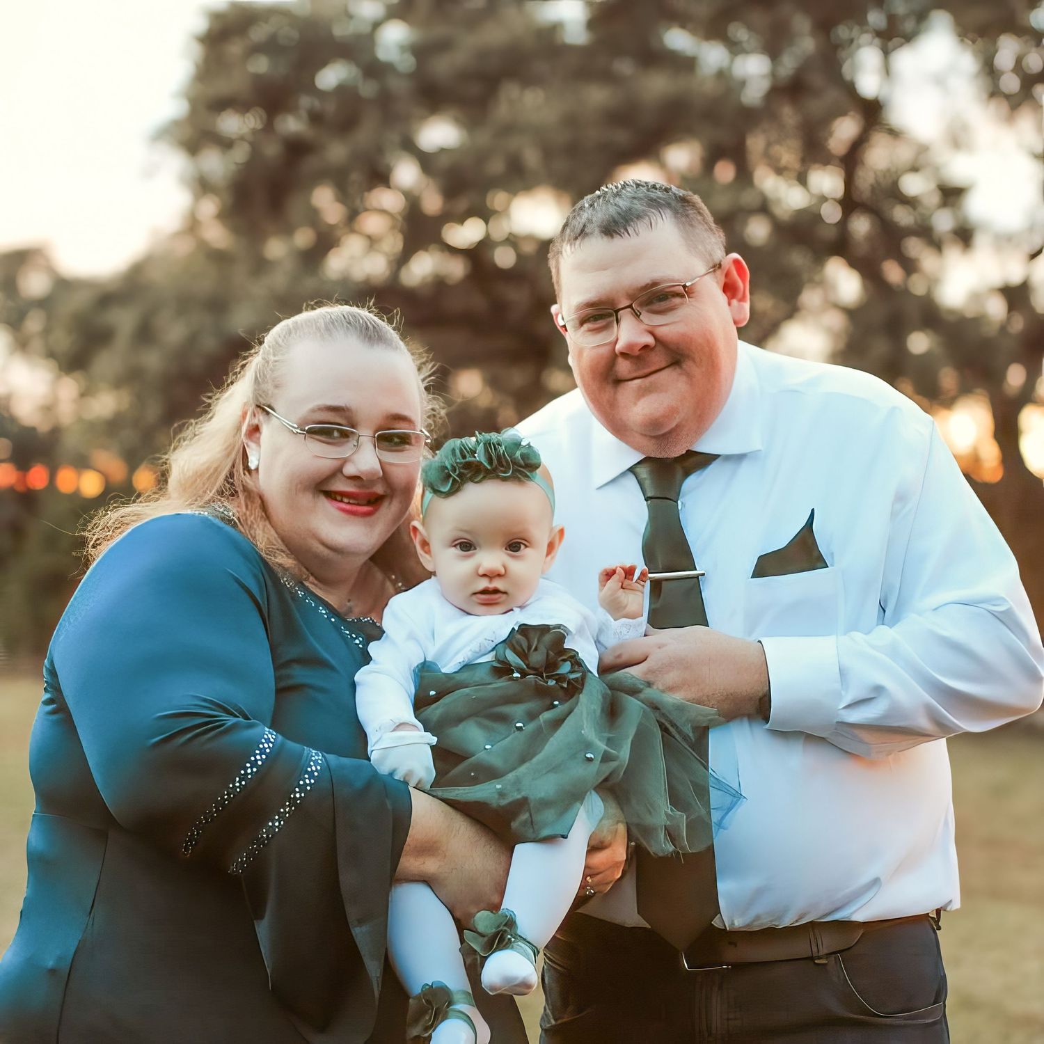 Husband and wife holding their female child, dressed up in green and white dress