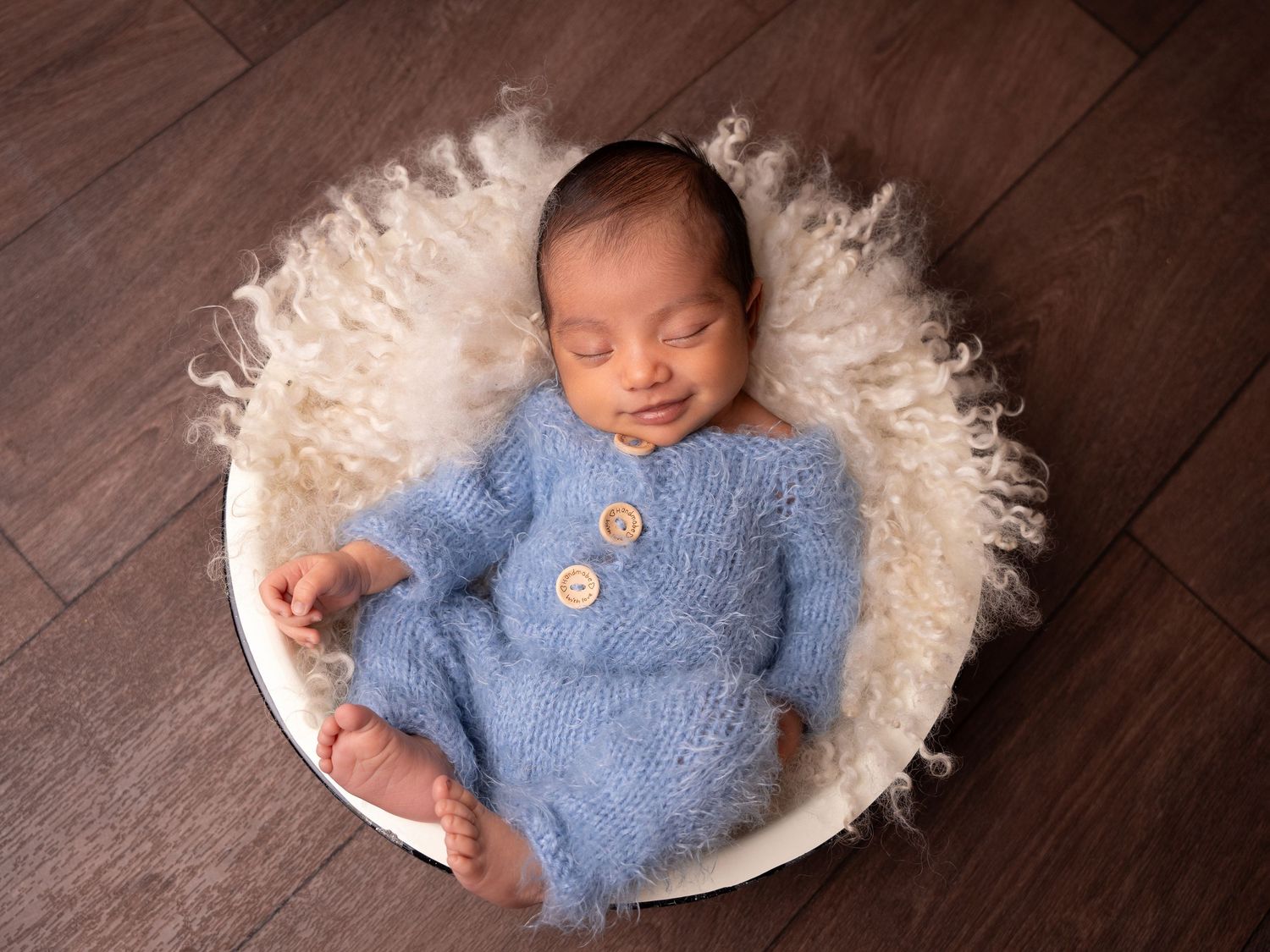 Baby boy sleeping on fluffy blanket snuggled in a bowl, in a cosy blue fluffy romper at newborn photoshoot in Doncaster.