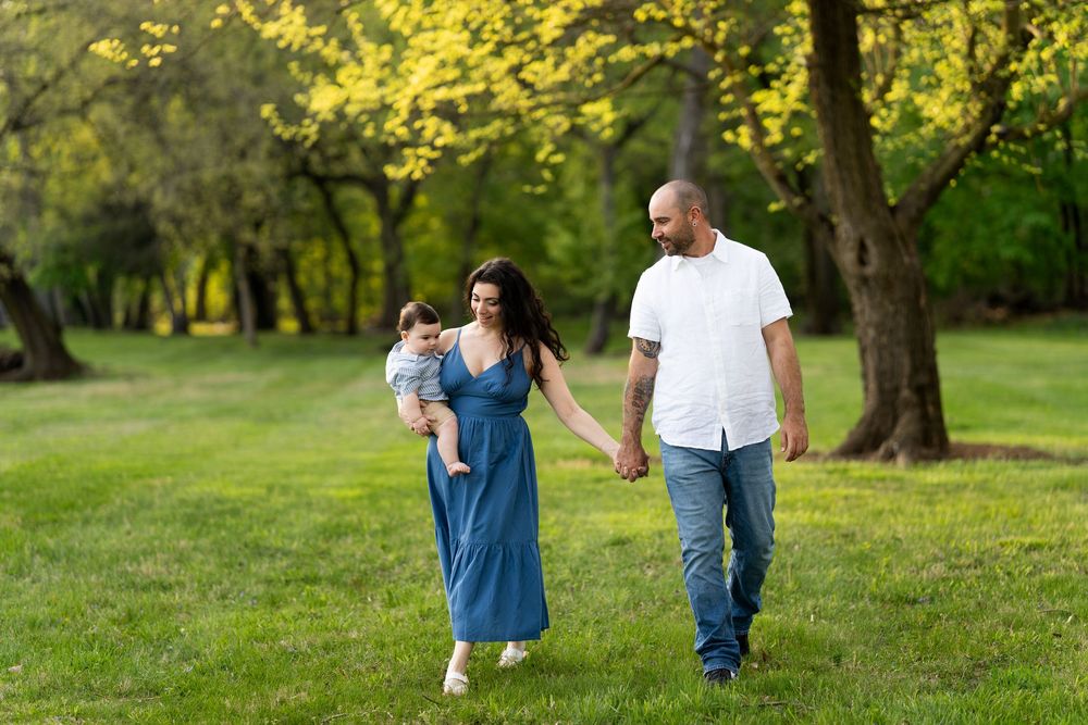 A couple and their baby walk together in spring during sunset in a lush green park.