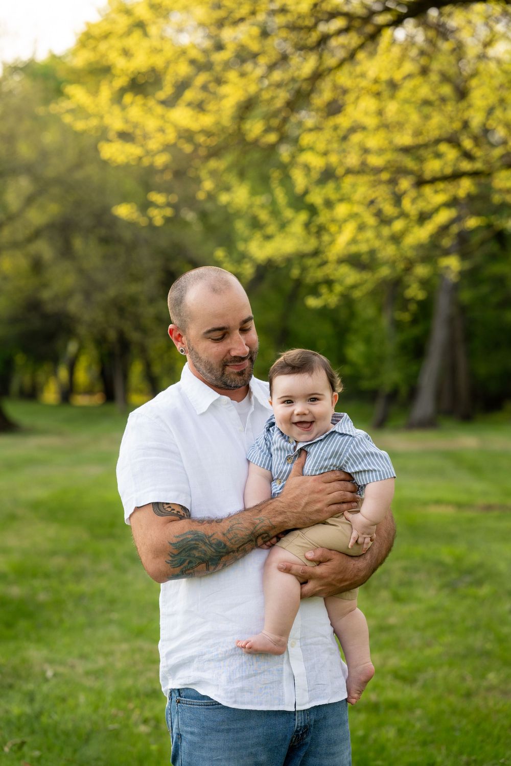 Parent and child share a joyful moment together in a sunlit park with green trees and grass in the background.