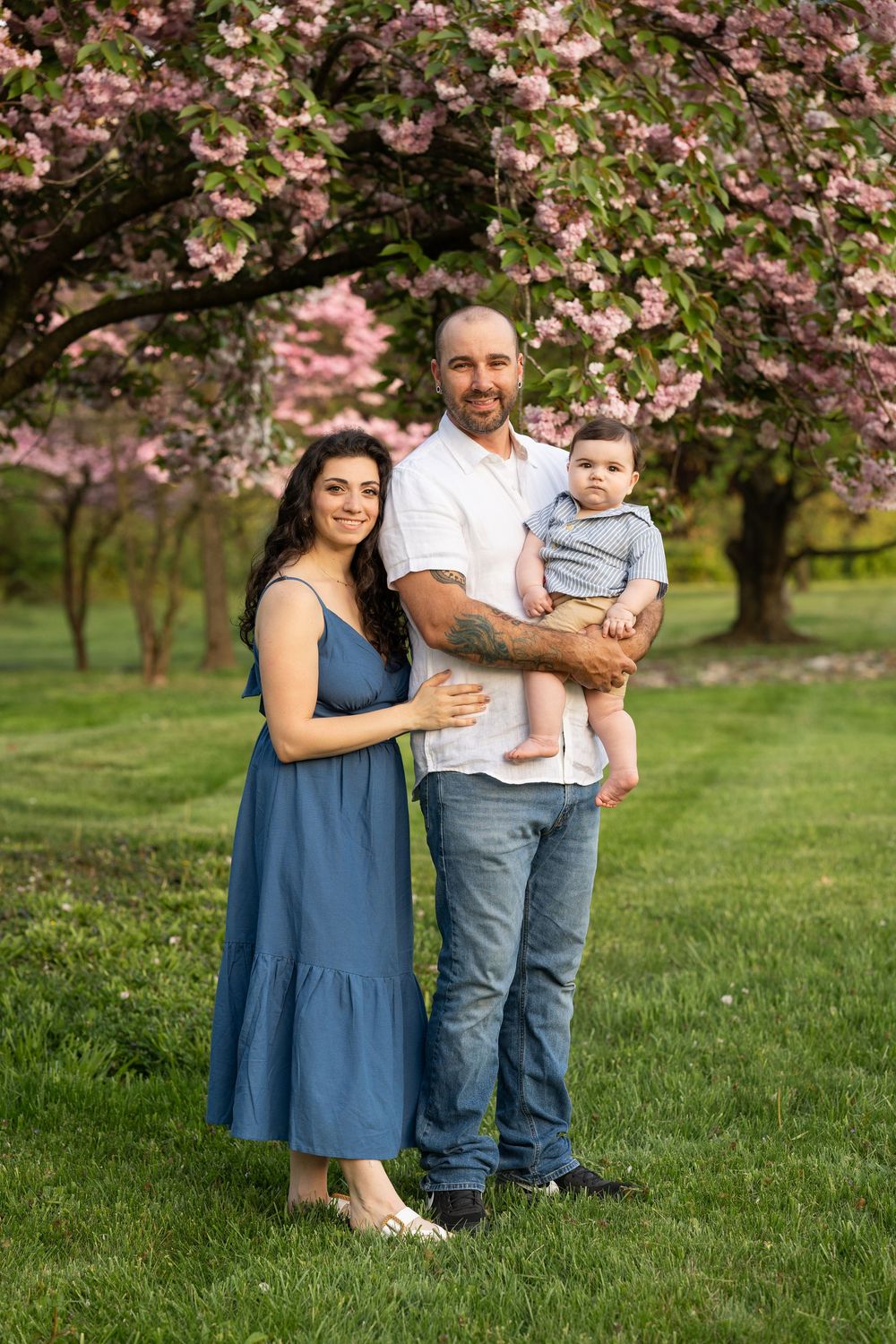 Family portrait under blooming pink cherry blossom trees in a spring garden setting at sunset.