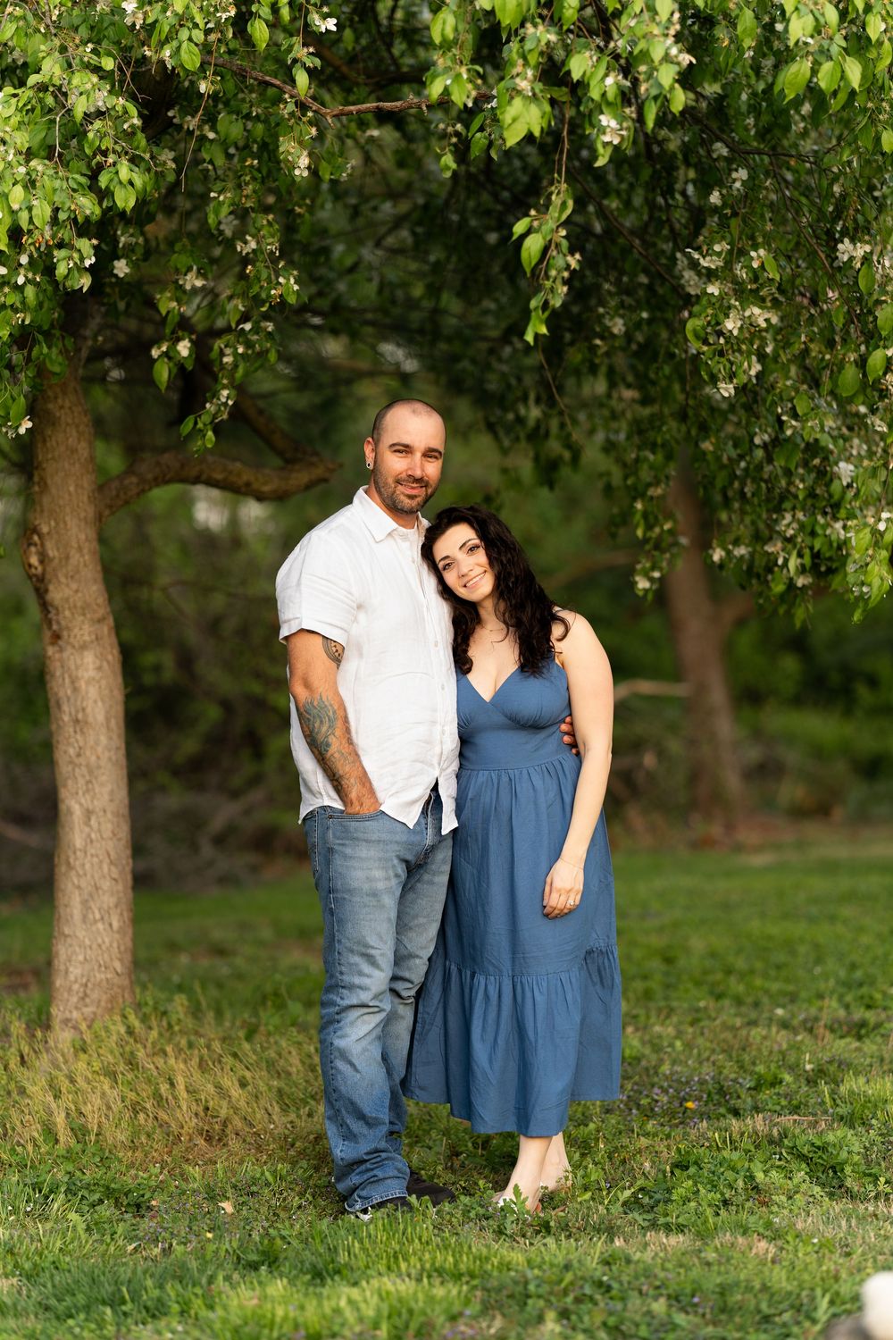 A couple stands together under blooming trees in a peaceful garden setting.