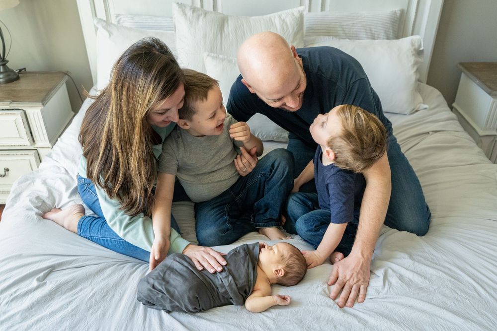 Family relaxing together on a cozy bed with light gray bedding in a bright bedroom setting.