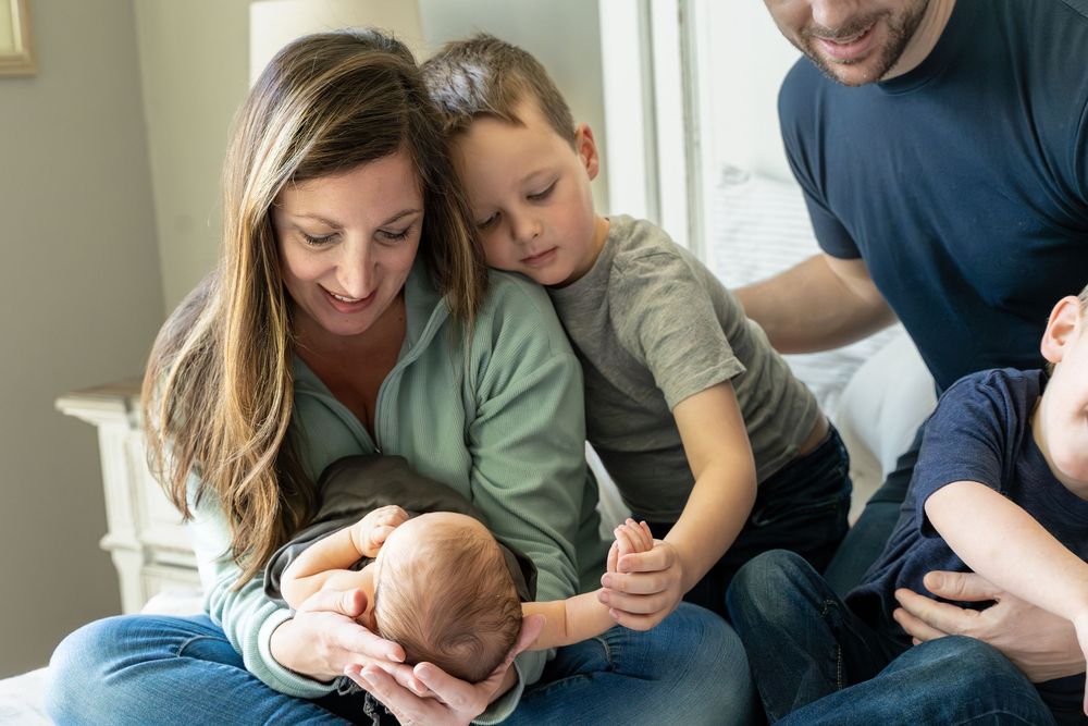 Family sits together on a couch while bonding with their baby in a bright room with natural lighting.