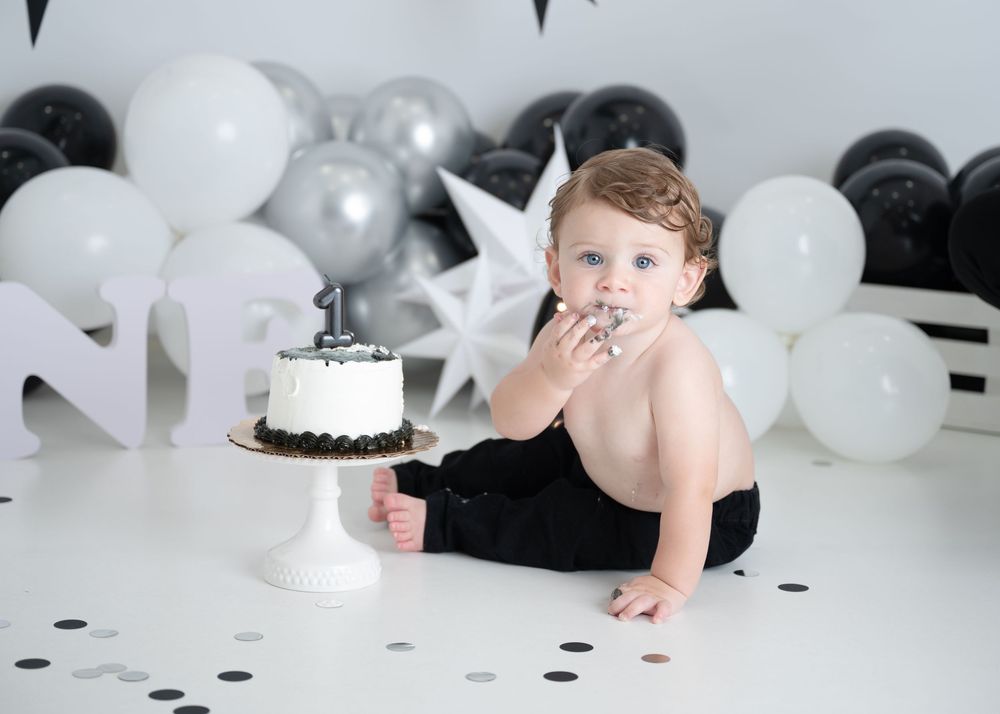 Black and white themed first birthday cake smash photo setup with balloons and stars in the background.