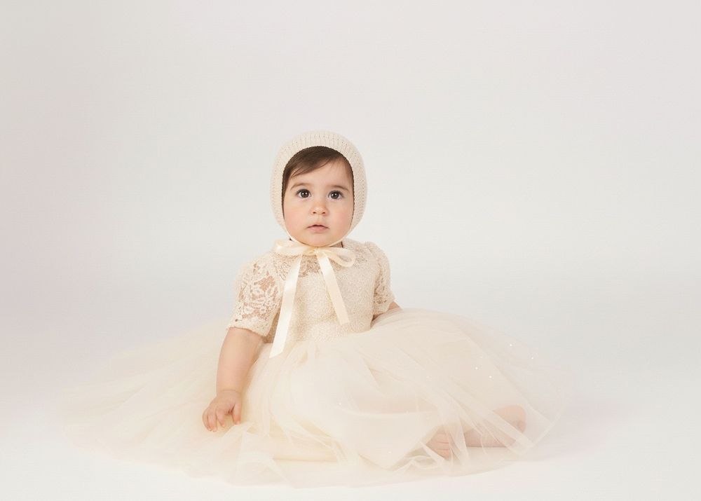 A baby in a cream-colored tulle dress poses for professional portraits in five similar poses on a light background.