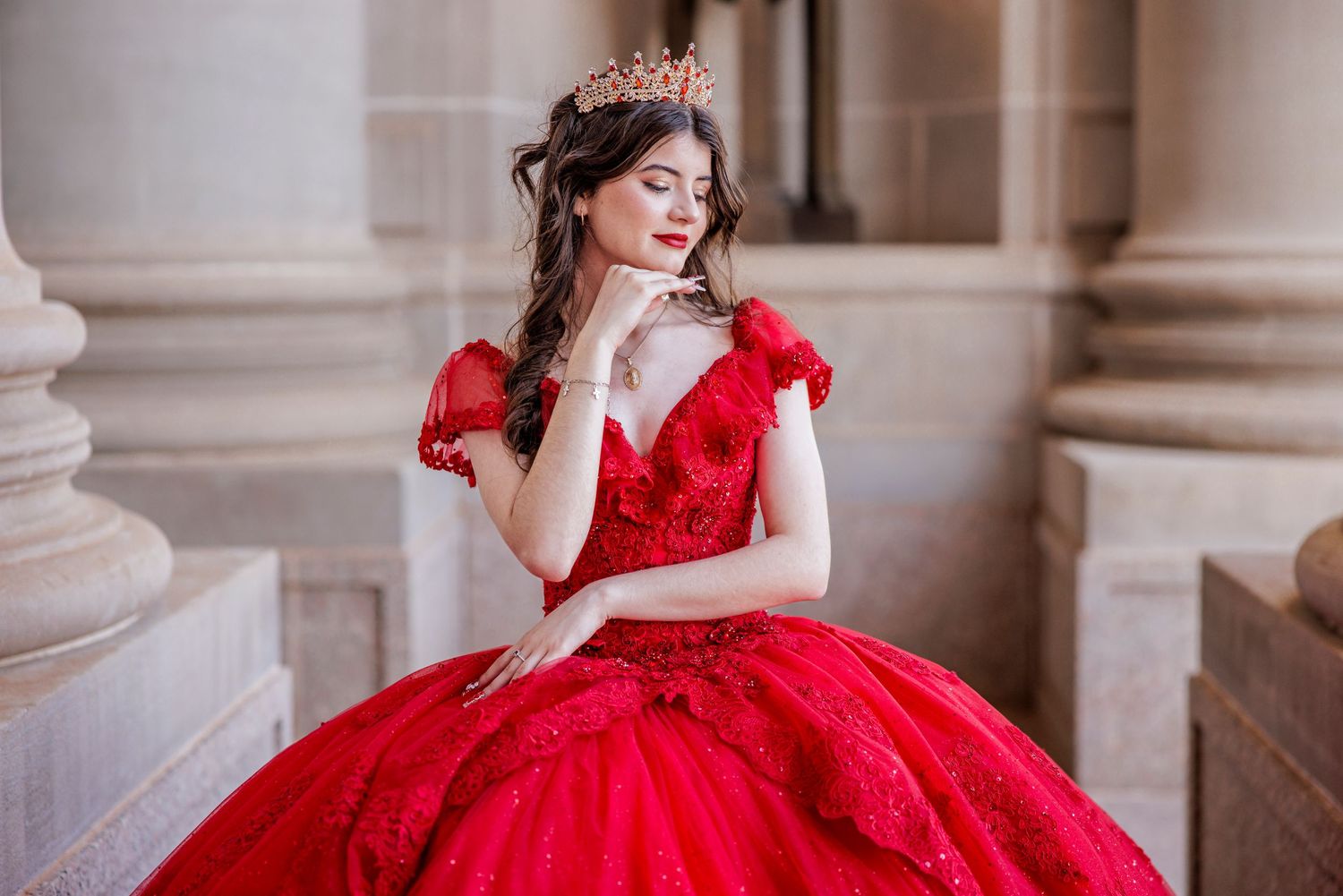An elegant red lace ball gown with flutter sleeves photographed against classical stone columns.