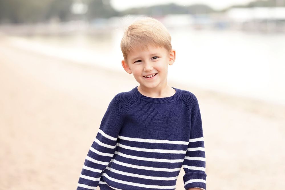 Two young boys in blue and white striped shirts playing at the beach.