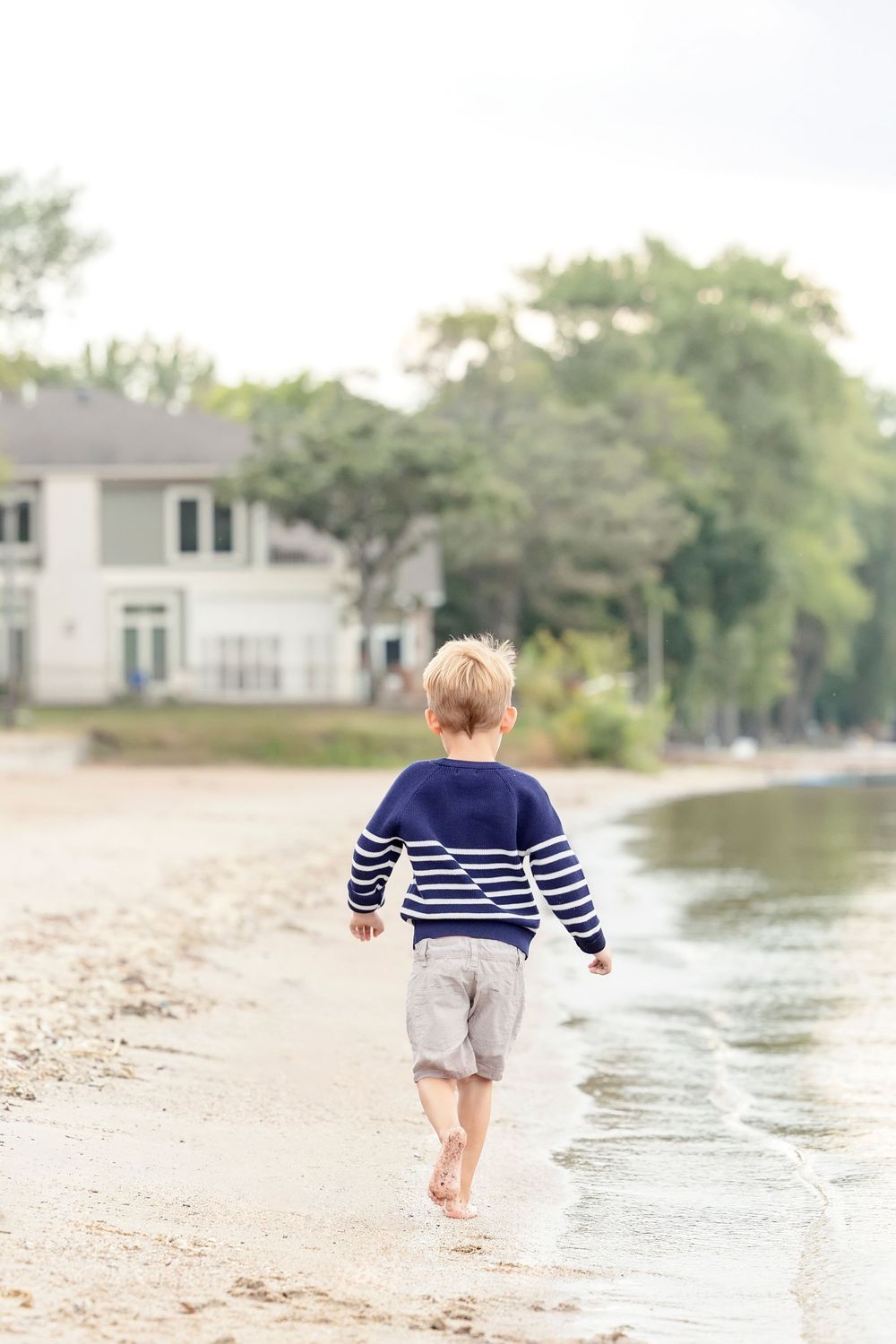 Child in navy striped shirt running along the beach shoreline.