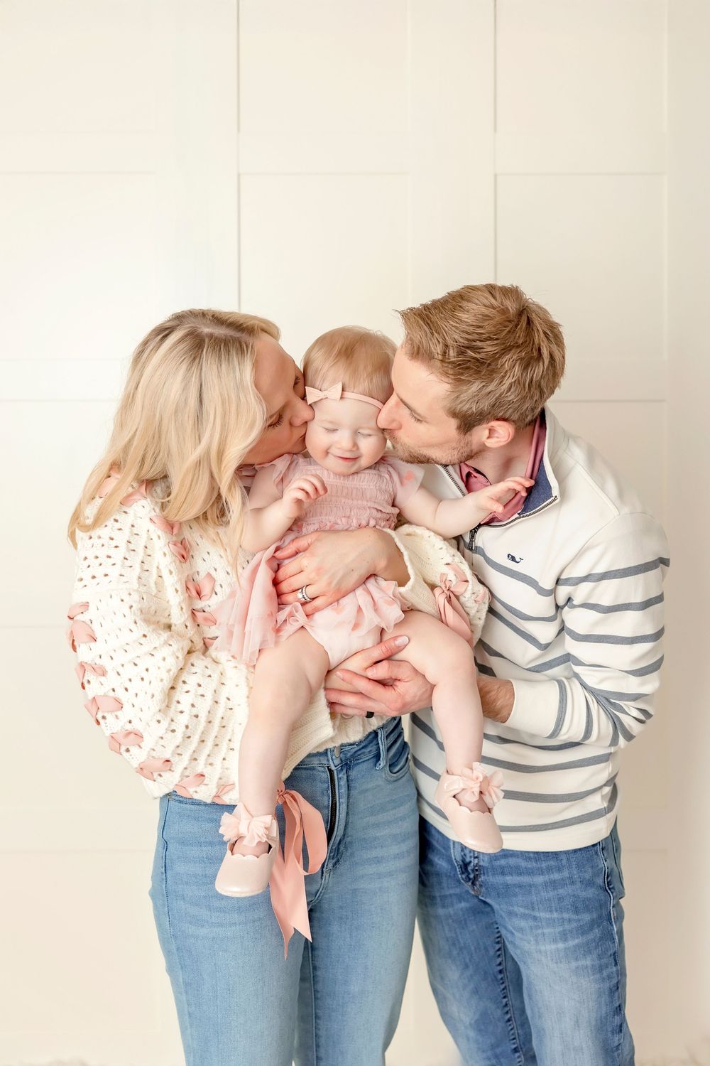 Family sharing loving kisses against white studio background in casual attire.