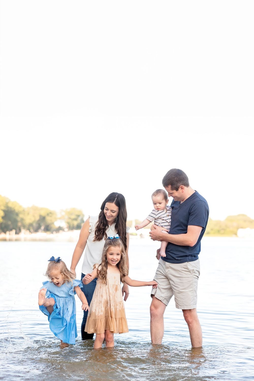 Family plays together in shallow water during sunset beach photo session.