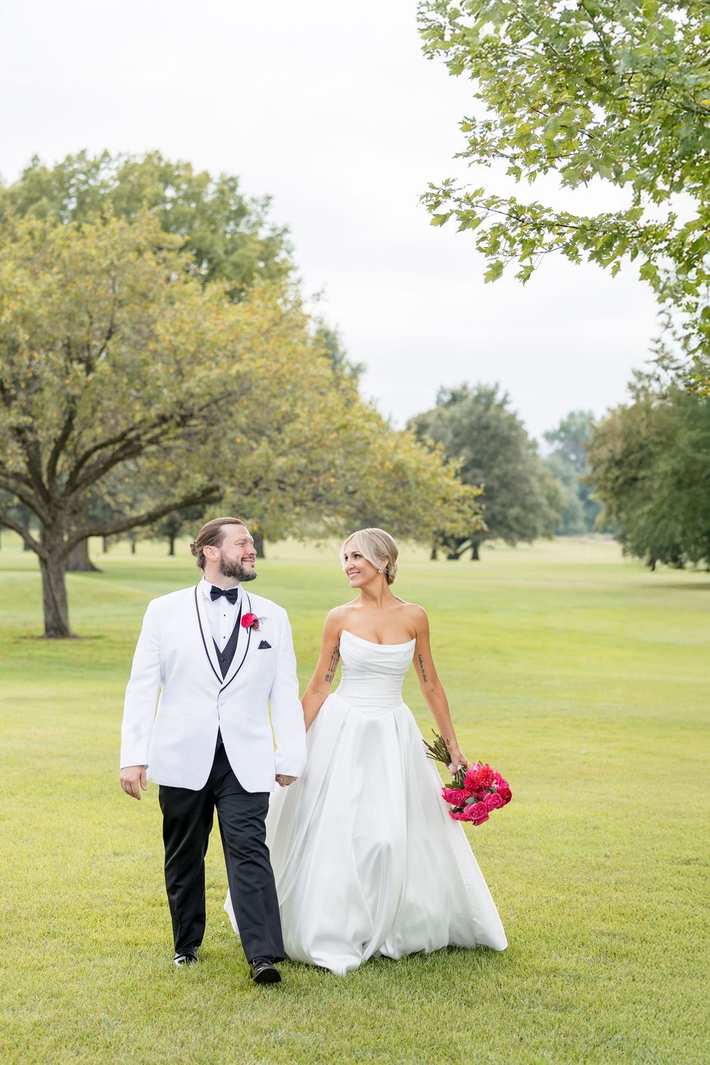 Wedding couple walking and posing together on a lush green lawn.