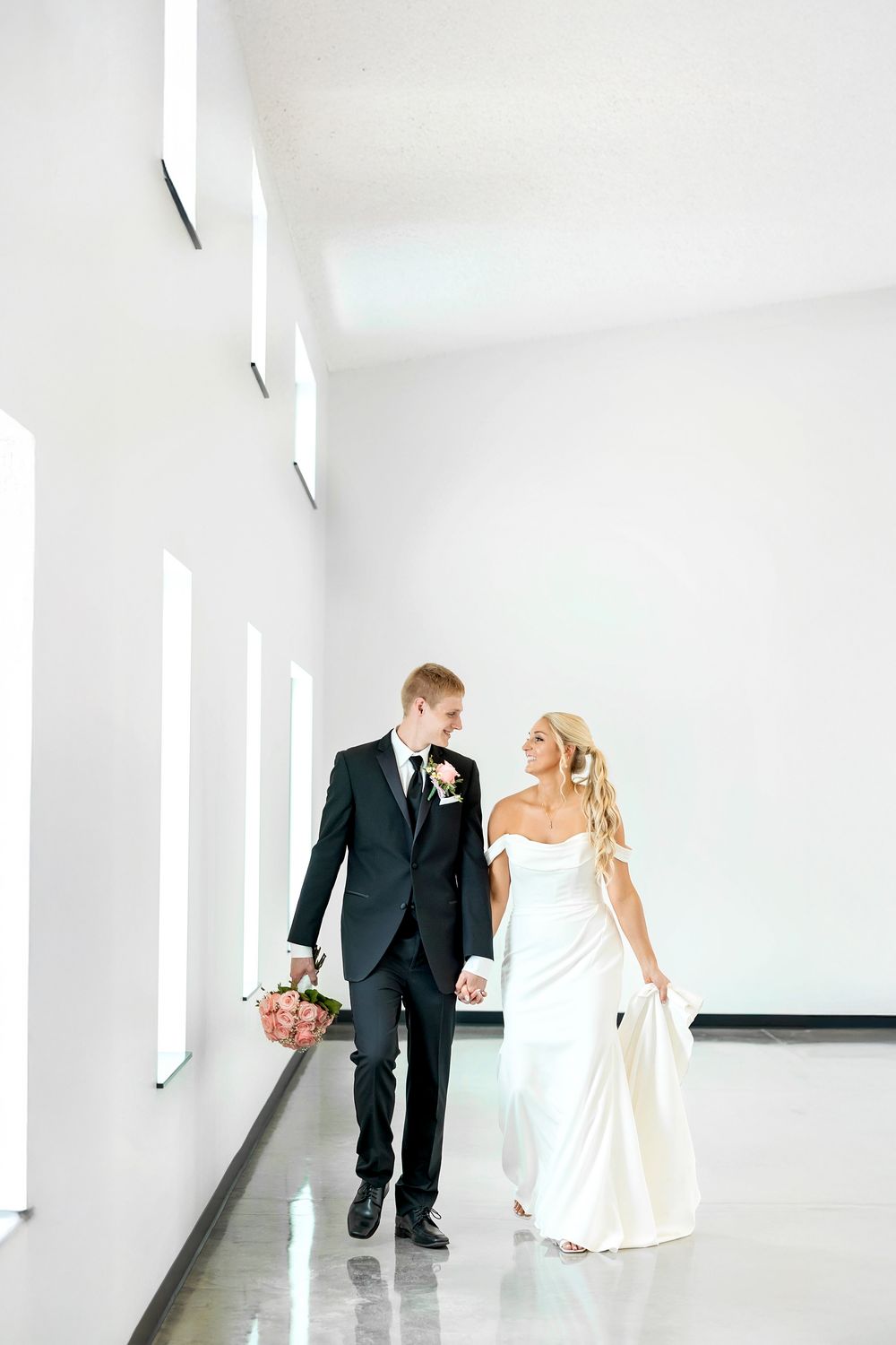Modern white corridor wedding portrait with dramatic natural lighting and minimalist design.