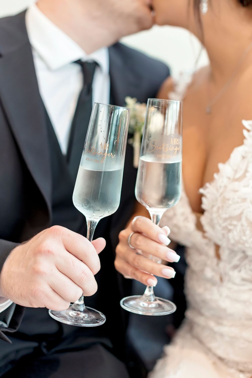 Close-up of bride and groom holding champagne glasses in formal wedding attire.