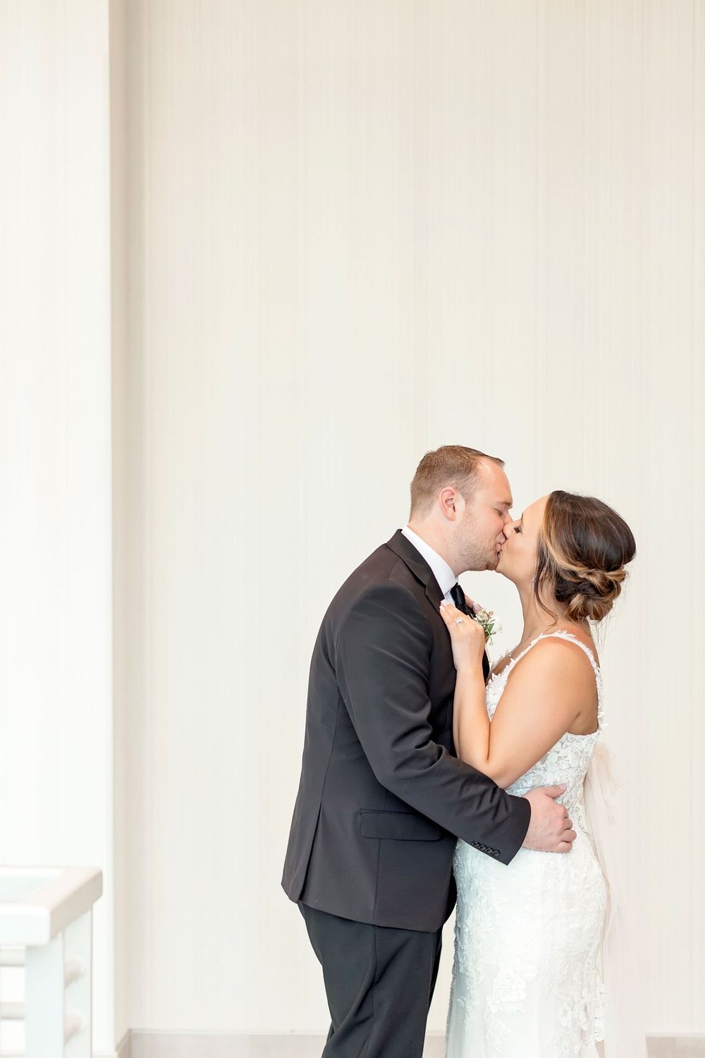 A romantic moment between newlyweds sharing their first kiss in an elegant white wedding venue.