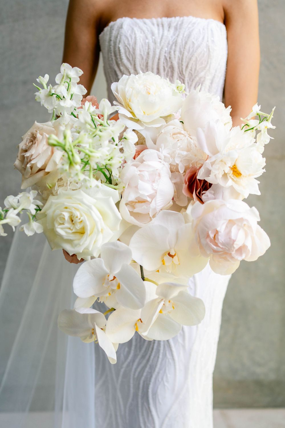 Elegant white and blush bridal bouquet featuring roses and orchids against textured wedding dress.