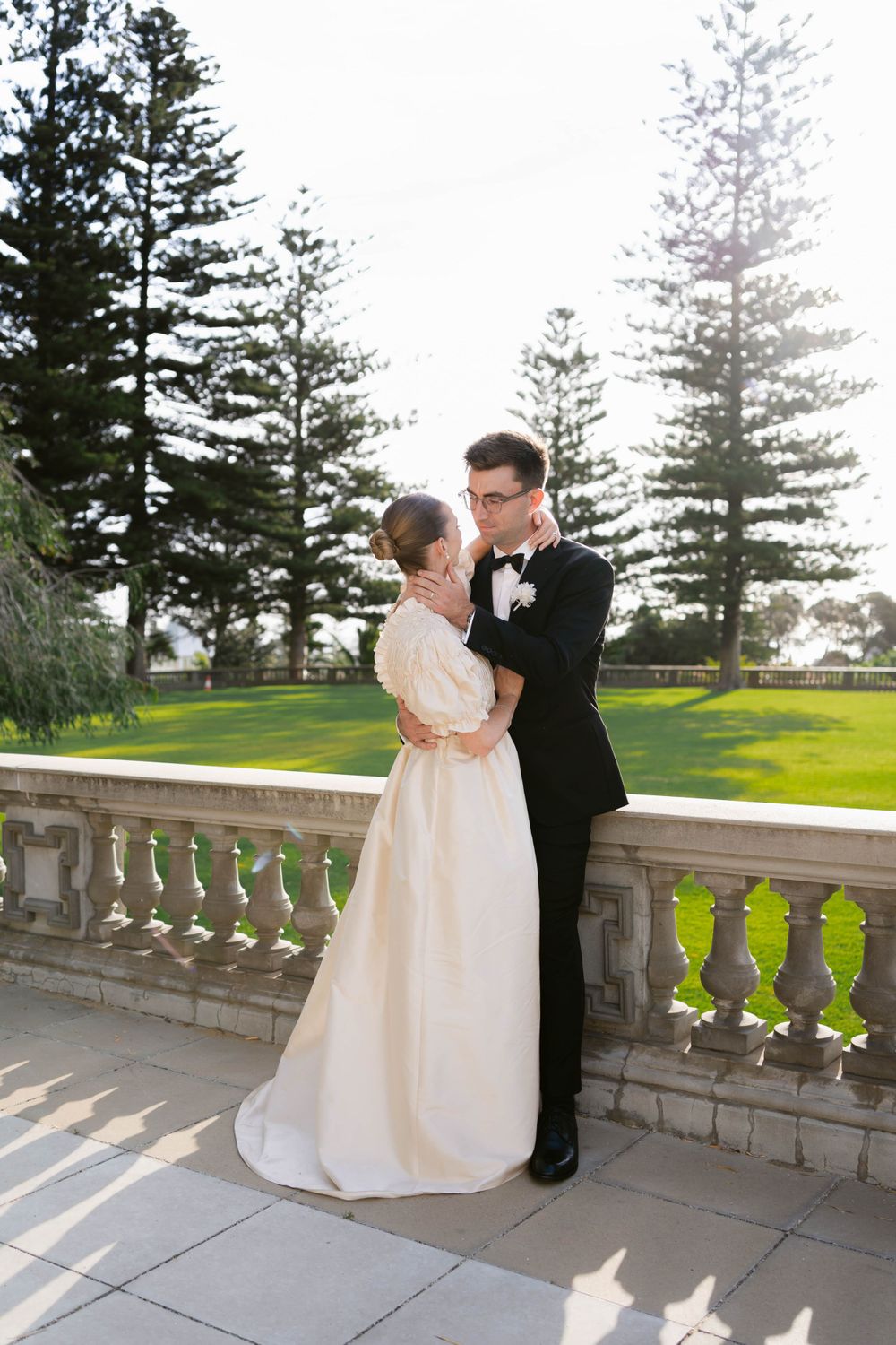 Romantic wedding portrait of couple embracing on an elegant stone terrace with pine trees.