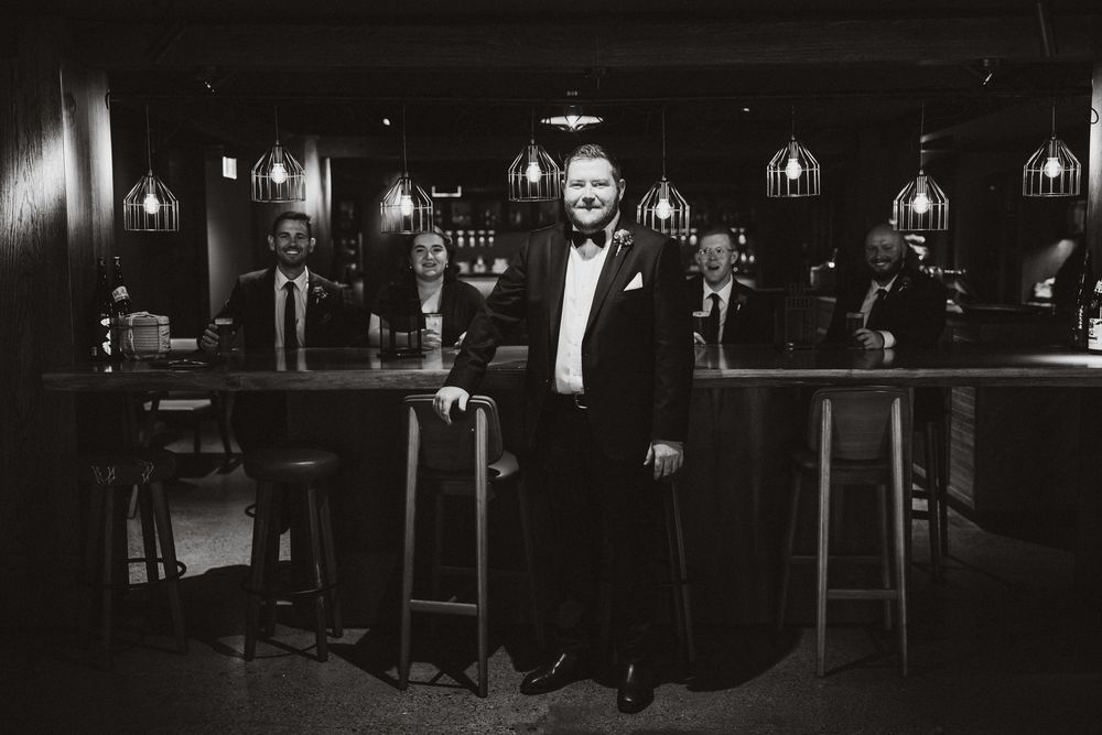 Black and white photo of elegantly dressed professionals posing in a stylish bar with pendant lights.