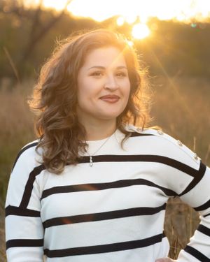 A person in a striped white sweater stands outdoors during golden hour sunset with backlit hair.