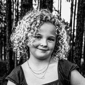 Black and white portrait of young child with natural curly blonde hair in forest setting.