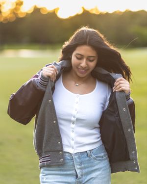 Someone in a white button-up top and denim enjoying a sunset outdoors while adjusting their navy jacket.