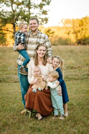 Family portrait outdoors in a field during golden hour sunset wearing casual attire in autumn.