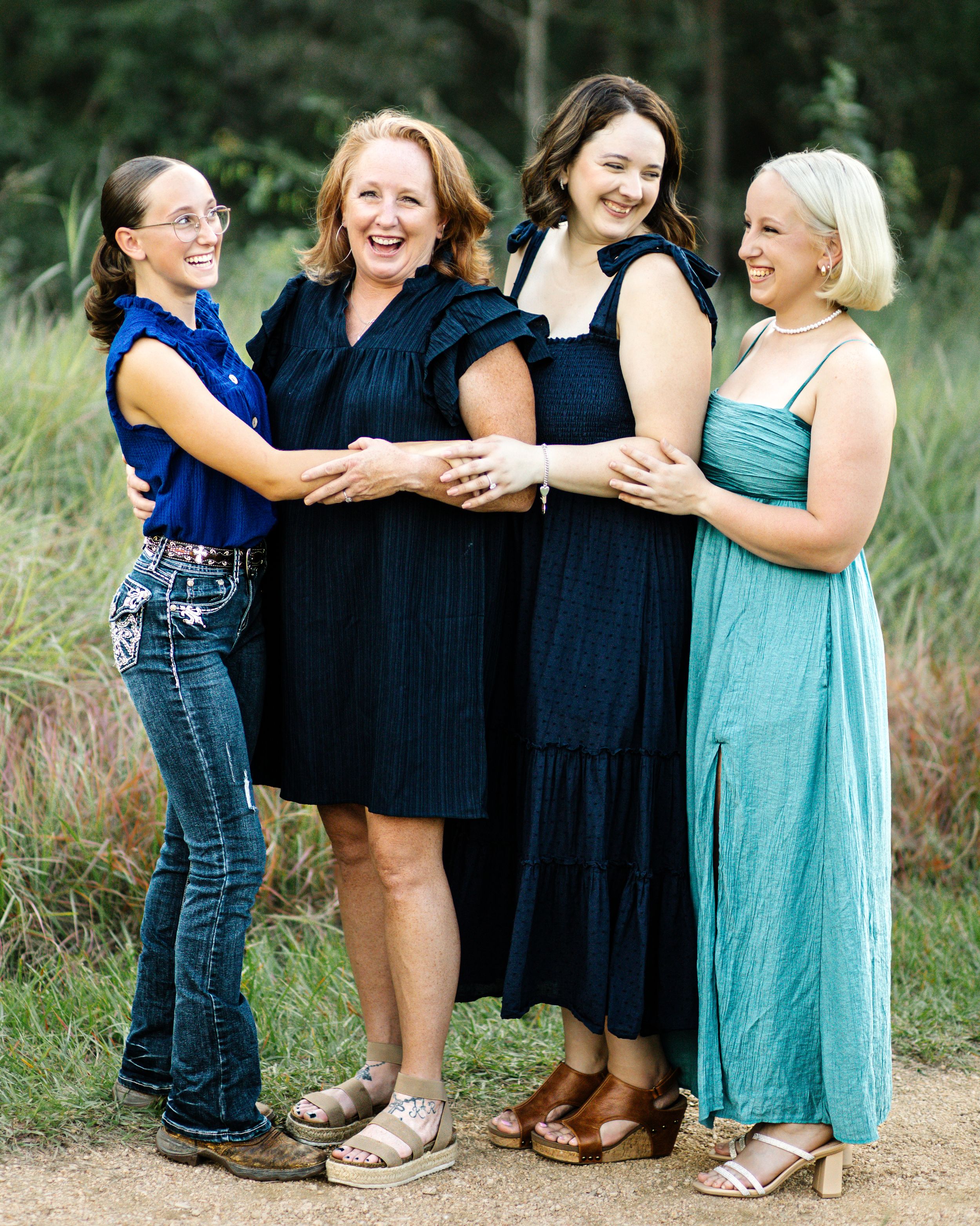 Four people in casual attire share joyful laughter together while standing outdoors in a grassy field.