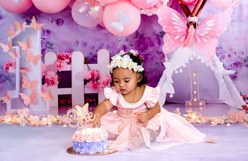 Pink and purple cake smash photo session with balloons and floral decorations for a first birthday celebration.